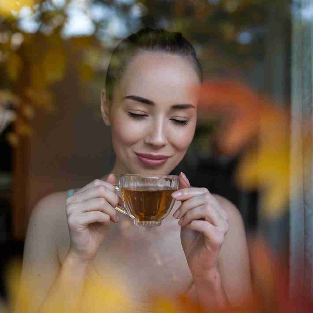Immagine di ragazza che bene il the alla finestra in scenario autunnale per l'articolo "Settembre senza sensi di colpa cosa imparare dall'estate"